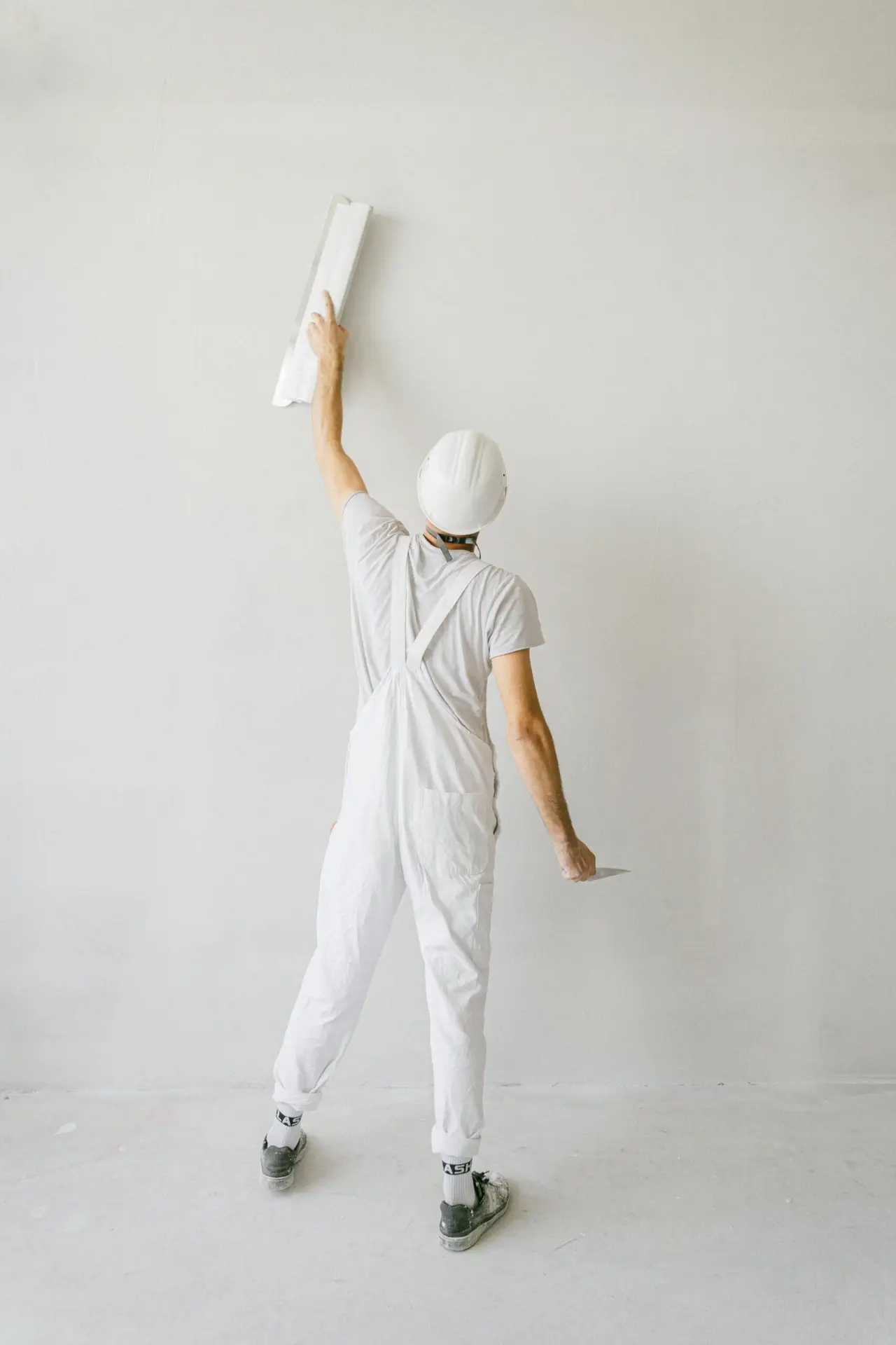 Back view of construction worker in overalls painting a wall white.